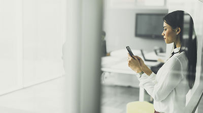 Applied Mobile Woman in business attire standing in an office while using a smart phone