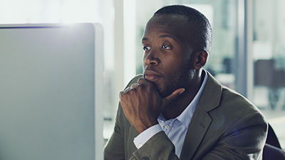 IVANS E-servicing Man dressed in business casual attire looking at computer screen with his chin resting in his hand.