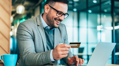 Young smiling businessman using credit card and laptop at modern office